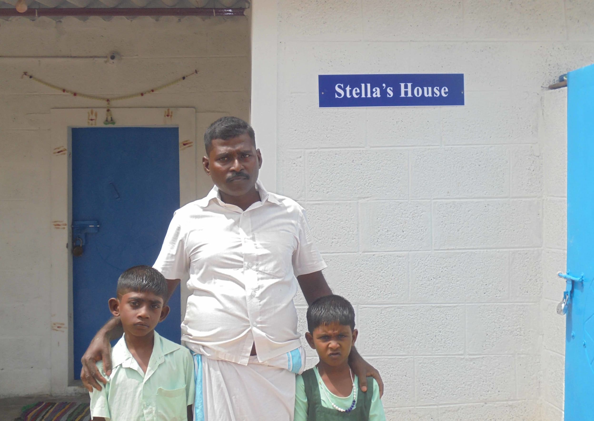 A father and his two children standing outside a house named Stella House